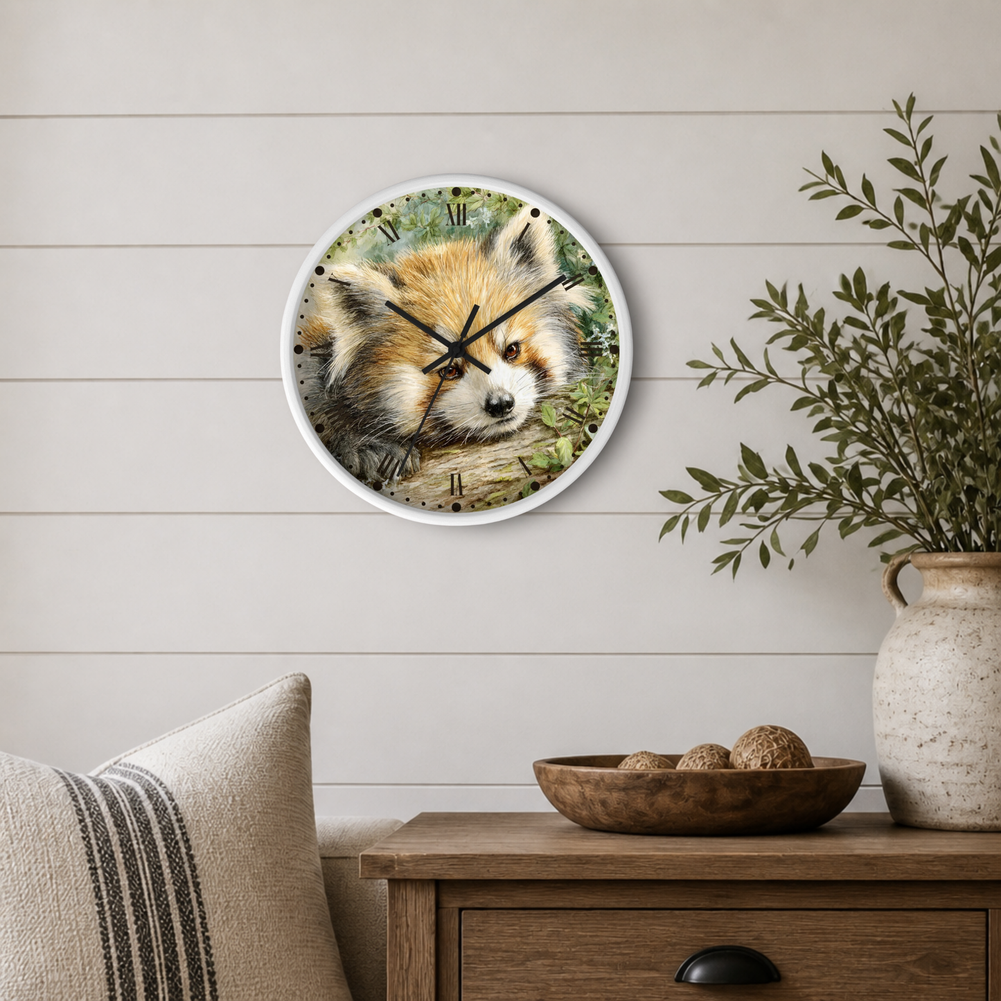A round wall clock with a white frame hangs on a light beige shiplap wall above a wooden side table. The clock face features a detailed illustration of a red panda resting in green foliage