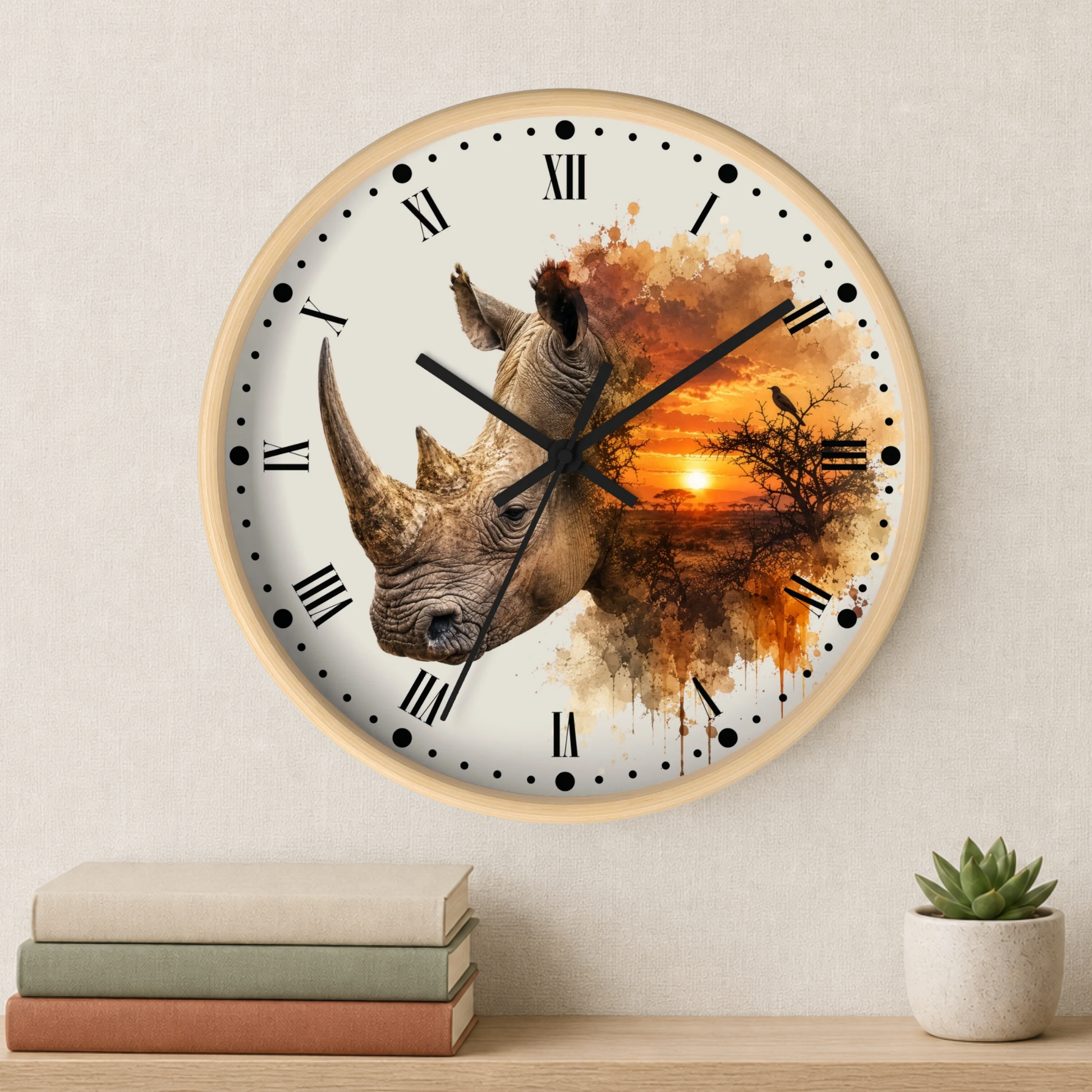 A round wall clock with a light wood frame and a printed design of a rhinoceros over an orange sunset landscape. The clock is mounted on a textured beige wall above a wooden shelf with stacked books and a small potted succulent.