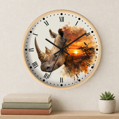 A round wall clock with a light wood frame and a printed design of a rhinoceros over an orange sunset landscape. The clock is mounted on a textured beige wall above a wooden shelf with stacked books and a small potted succulent.