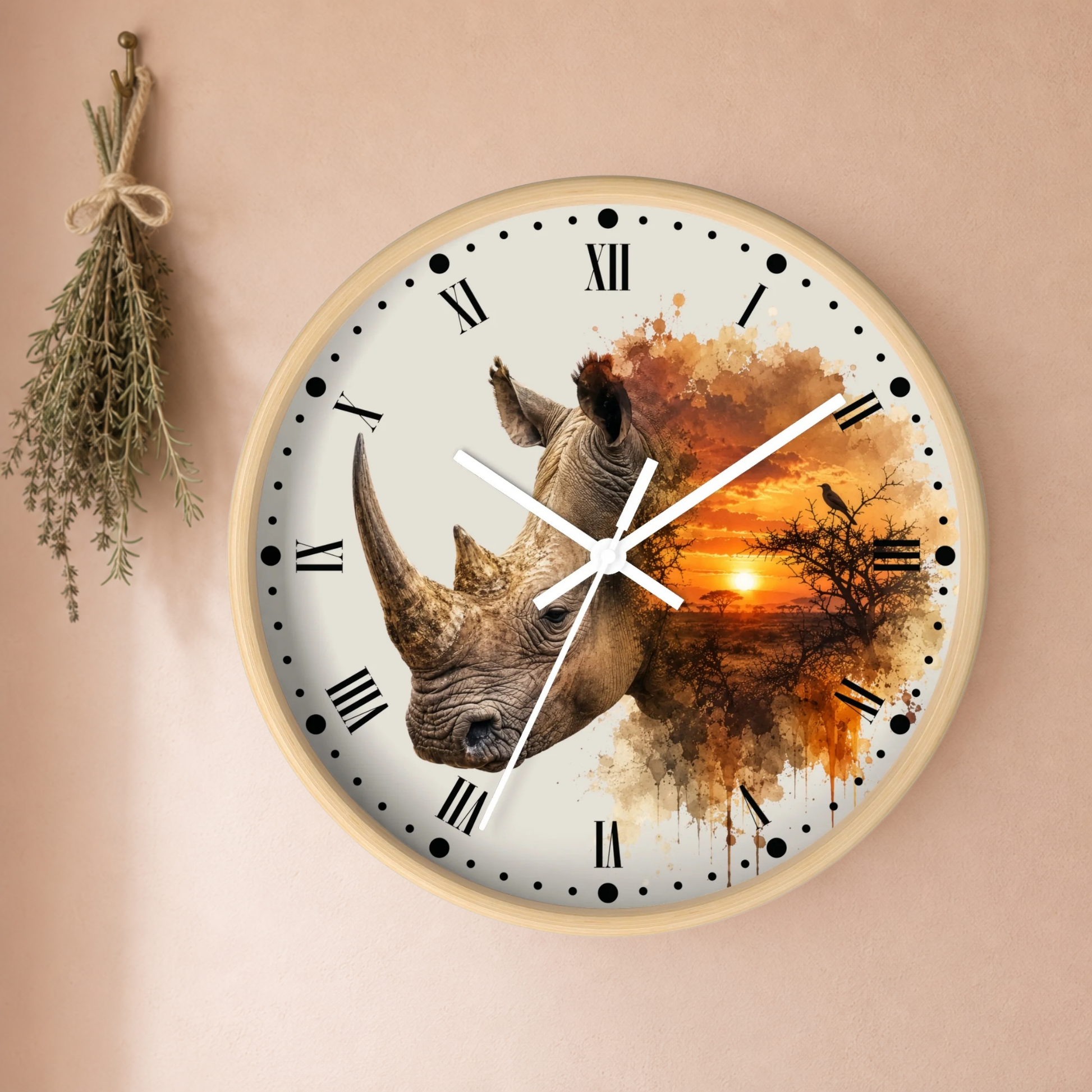 A round wall clock with a light wood frame, featuring a rhinoceros and sunset landscape print on the face, mounted on a beige wall with a dried herb sprig hanging to the left.