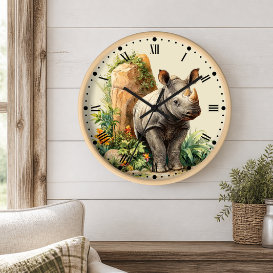 A round wall clock with a light wood frame hangs on a white shiplap wall above a wooden table. The clock face features a detailed illustration of a gray rhinoceros standing among green foliage and rocks, with black Roman numerals and hands.