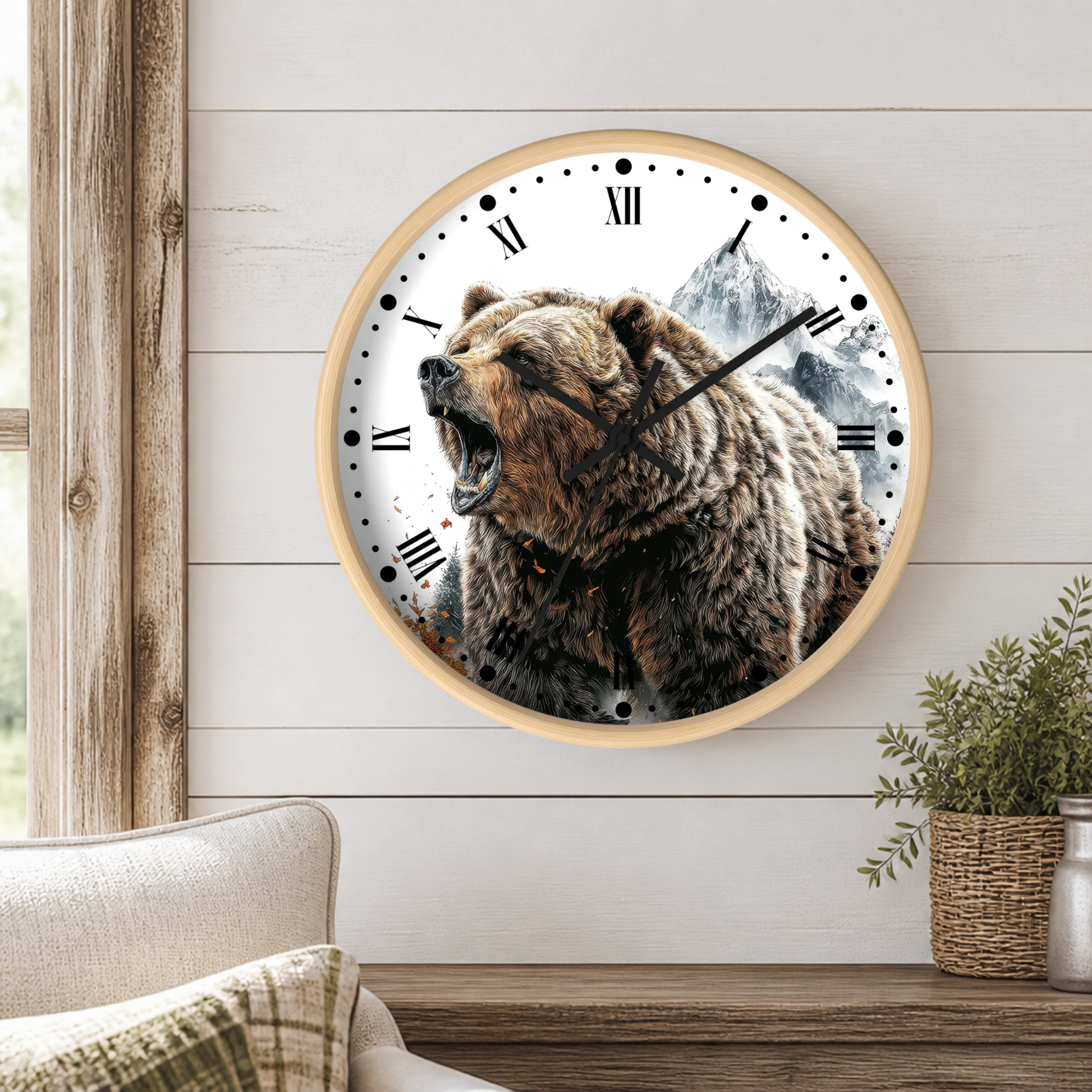 A round wall clock with a light wood frame hangs on a white shiplap wall above a wooden table. The clock face features a detailed graphic of a roaring brown bear in front of a mountain landscape, with black Roman numerals and hands.