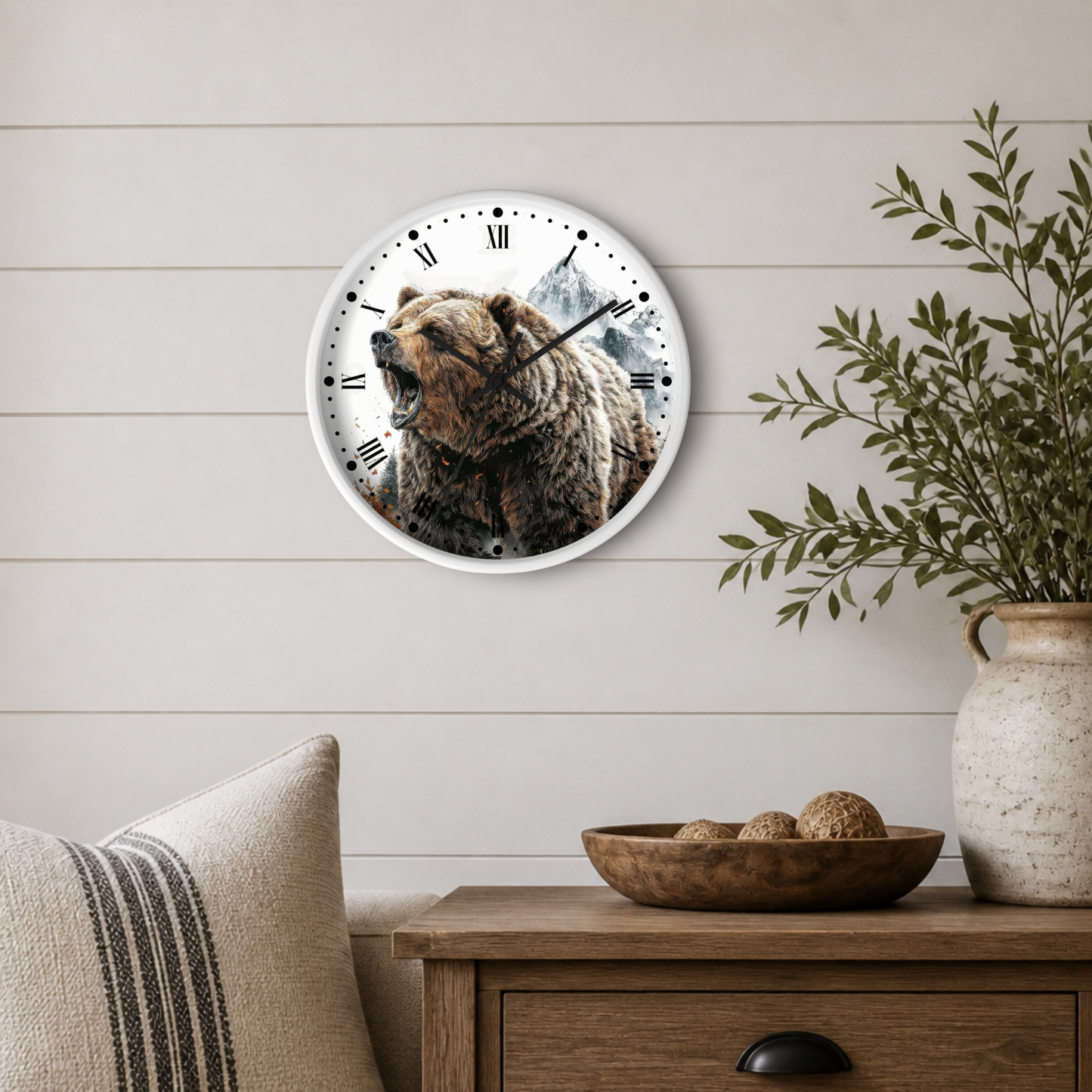 A round wall clock with a grizzly bear illustration and Roman numerals, mounted on a light wood paneled wall above a wooden side table with a plant and decorative bowl.
