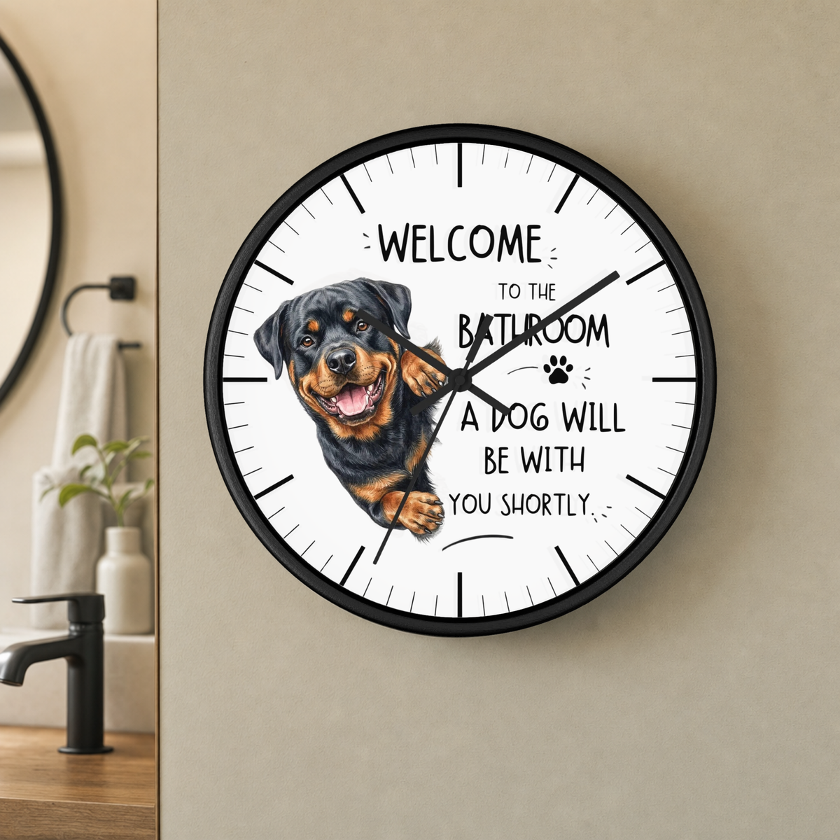 A round wall clock with a black frame and a white face featuring a Rottweiler dog illustration and the text 'WELCOME TO THE BATHROOM A DOG WILL BE WITH YOU SHORTLY'. The clock is mounted on a beige wall in a bathroom setting.