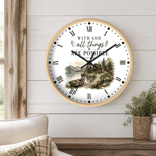 A round wall clock with a light wood frame hangs on a white shiplap wall above a wooden table. The clock face features a scenic landscape illustration of a lake and cabin, with the text 'WITH GOD all things ARE POSSIBLE' and 'LAWSON'S TONIGHTS' printed on it.