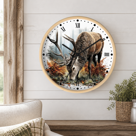 A round wall clock with a light wood frame hangs on a white shiplap wall above a wooden mantel. The clock face features a detailed illustration of a elk with large antlers in an autumn forest scene.
