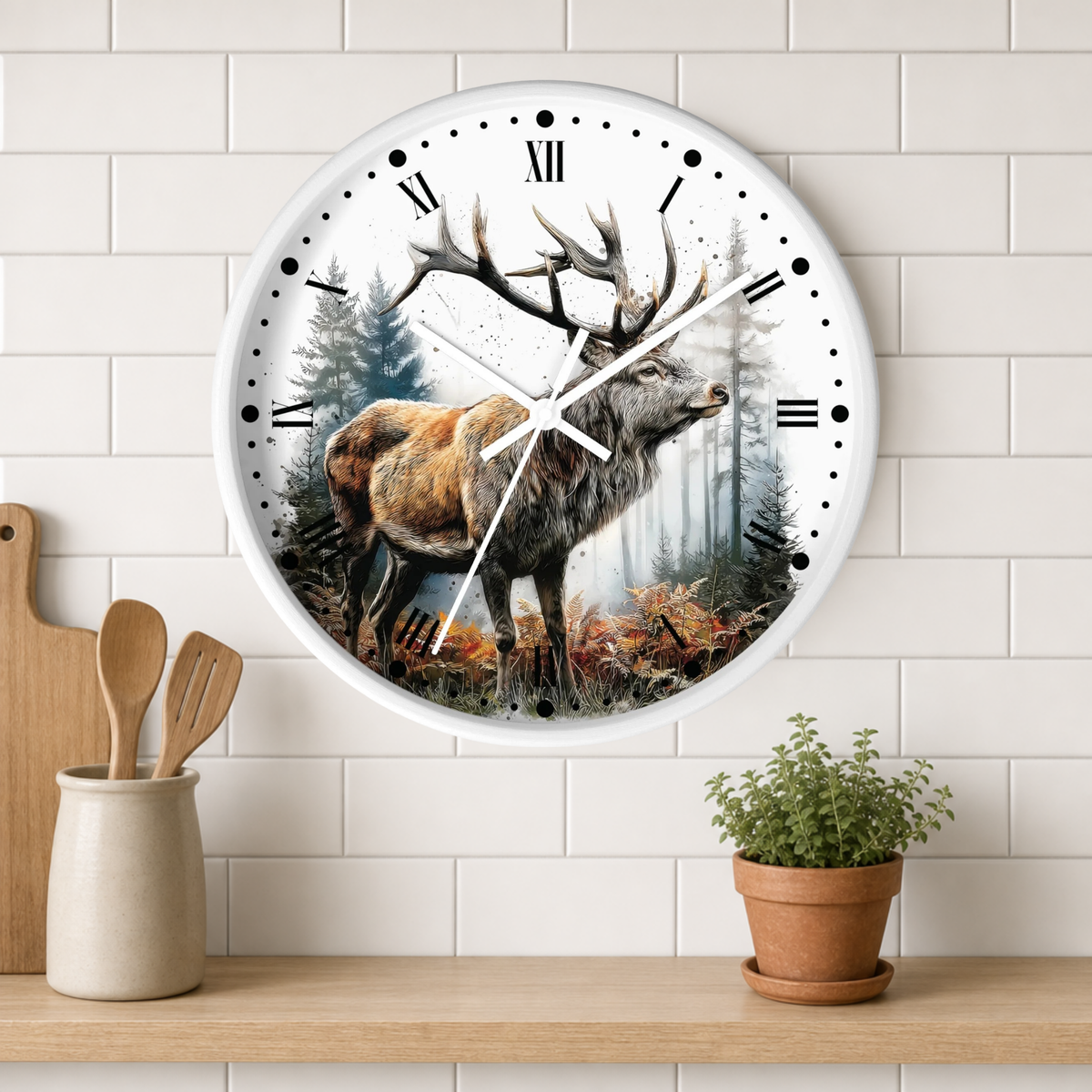 A round wall clock with a white frame and Roman numerals, featuring a painted stag in a misty forest on the face. The clock is mounted on a white subway-tile wall above a wooden shelf with a small potted plant and wooden utensils.