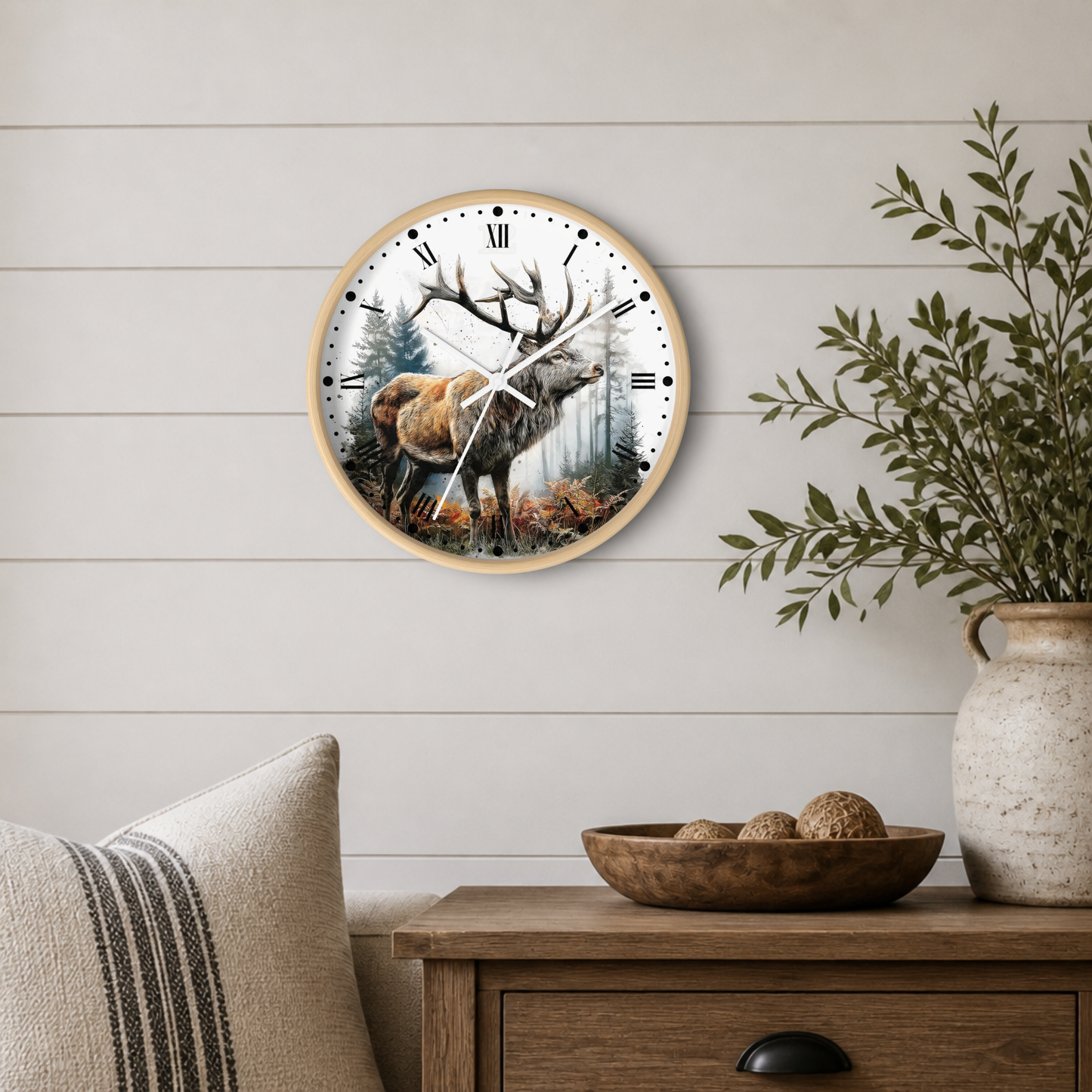 A round wall clock with a natural wood frame hangs on a white shiplap wall above a wooden side table. The clock face features a detailed illustration of a deer in a forest.