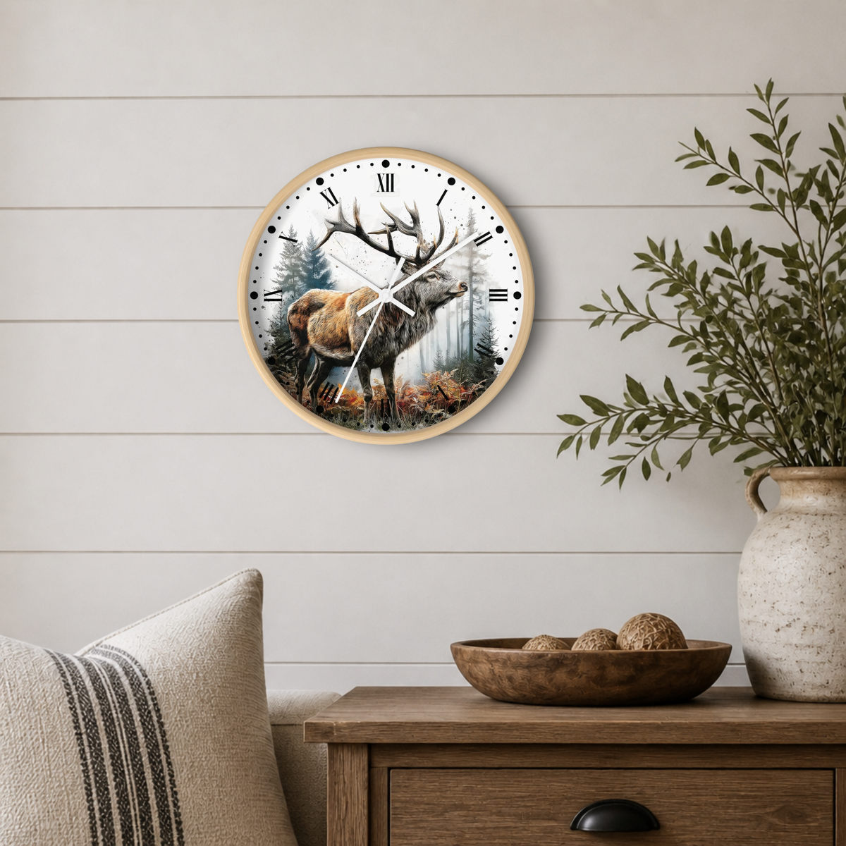 A round wall clock with a natural wood frame hangs on a white shiplap wall above a wooden side table. The clock face features a detailed illustration of a deer in a forest.