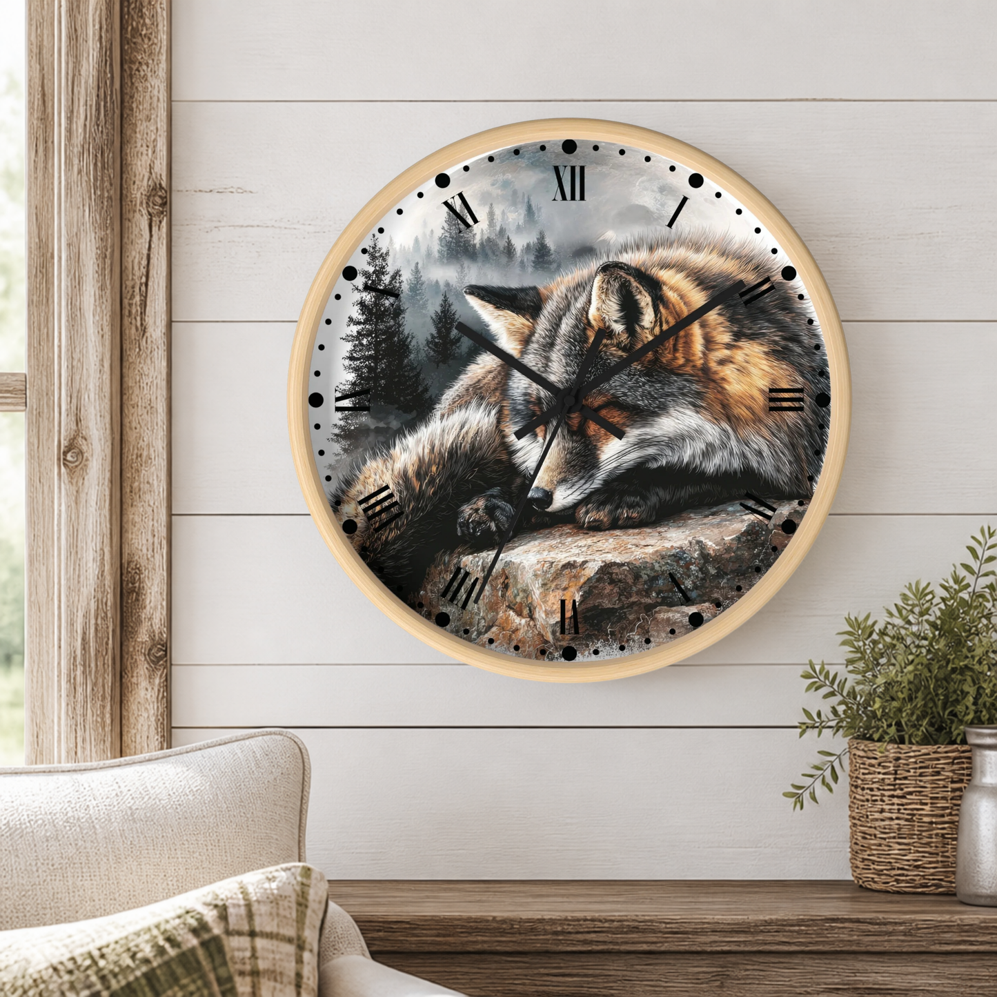 A round wall clock with a light wood frame hangs on a white shiplap wall above a wooden table. The clock face features a detailed illustration of a sleeping fox in a forest scene.