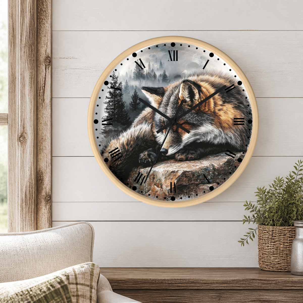 A round wall clock with a light wood frame hangs on a white shiplap wall above a wooden table. The clock face features a detailed illustration of a sleeping fox in a forest scene.