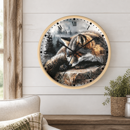 A round wall clock with a light wood frame hangs on a white shiplap wall above a wooden table. The clock face features a detailed illustration of a sleeping fox in a forest scene.
