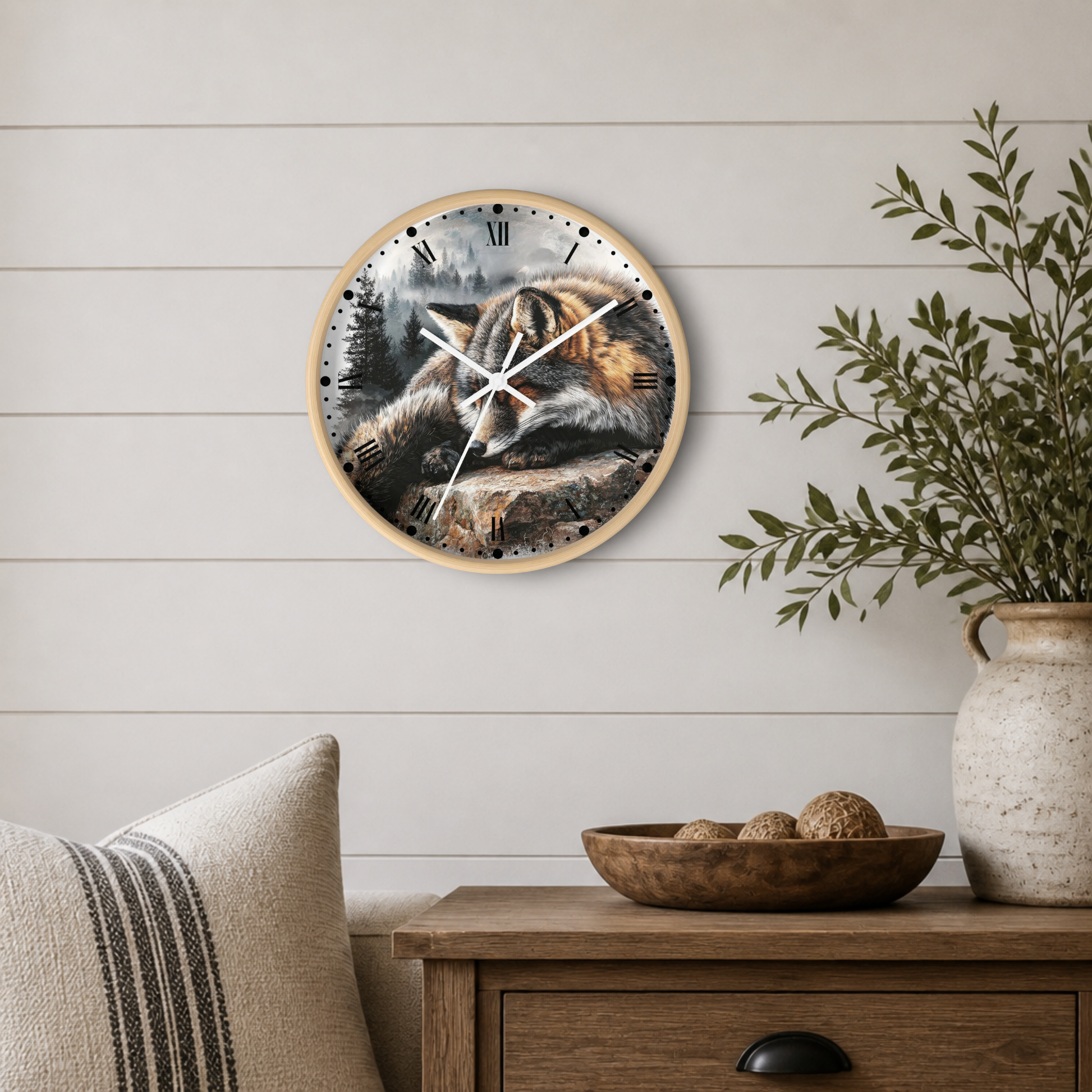 Round wall clock with a natural wood frame and a detailed illustration of a fox sleeping on a log, mounted on a white shiplap wall above a wooden side table with a plant and decorative items.