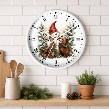 A round wall clock with a white face and black Roman numerals, featuring an illustration of a gnome, a snowman, and a bear among pine trees. The clock is mounted on a white subway tile wall above a wooden shelf styled with kitchen utensils, a candle, pinecones, and a potted plant.