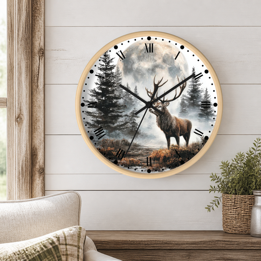 A round wall clock with a light wood frame hangs on a white shiplap wall above a wooden table. The clock face features a scenic illustration of a stag in a forest under a full moon.
