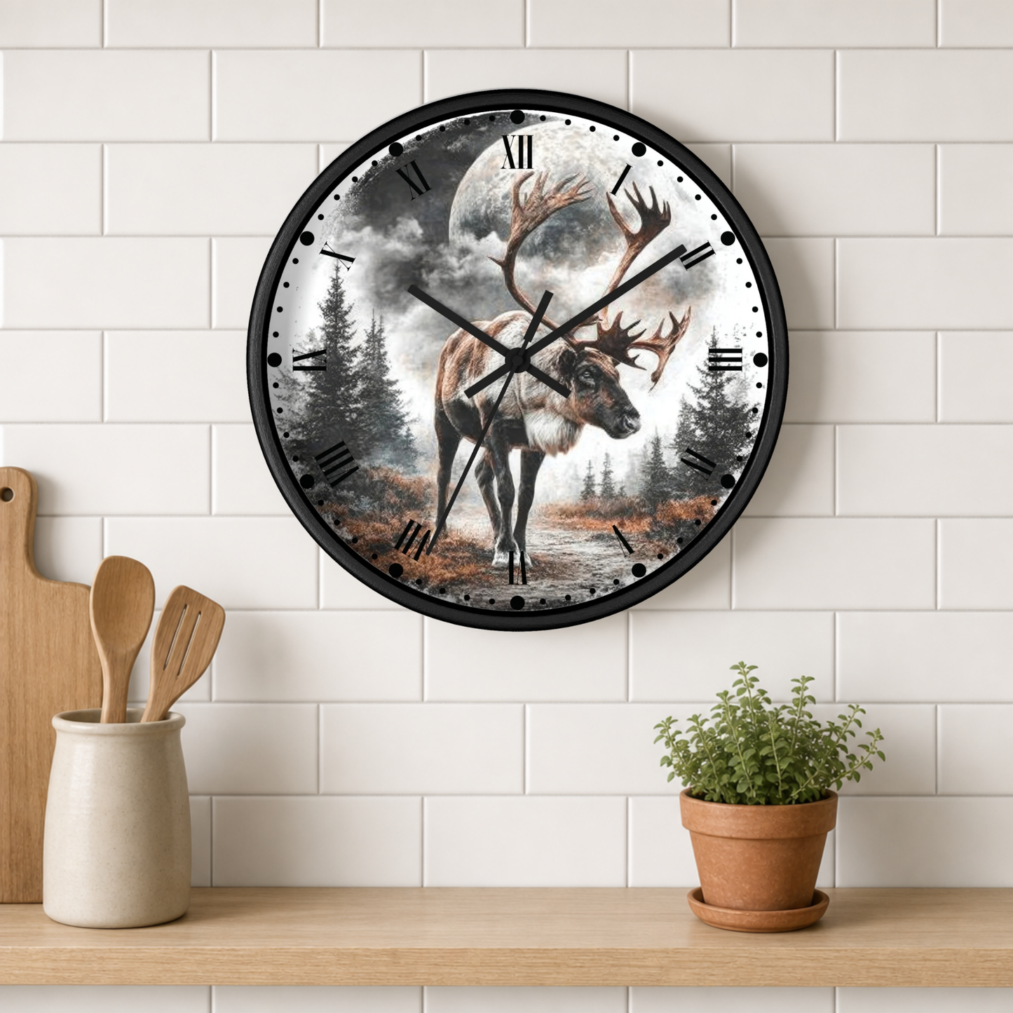 A round wall clock with a black frame hangs on a white subway tile wall above a wooden shelf. The clock face features a detailed illustration of a stag with large antlers standing in a forest under a full moon.