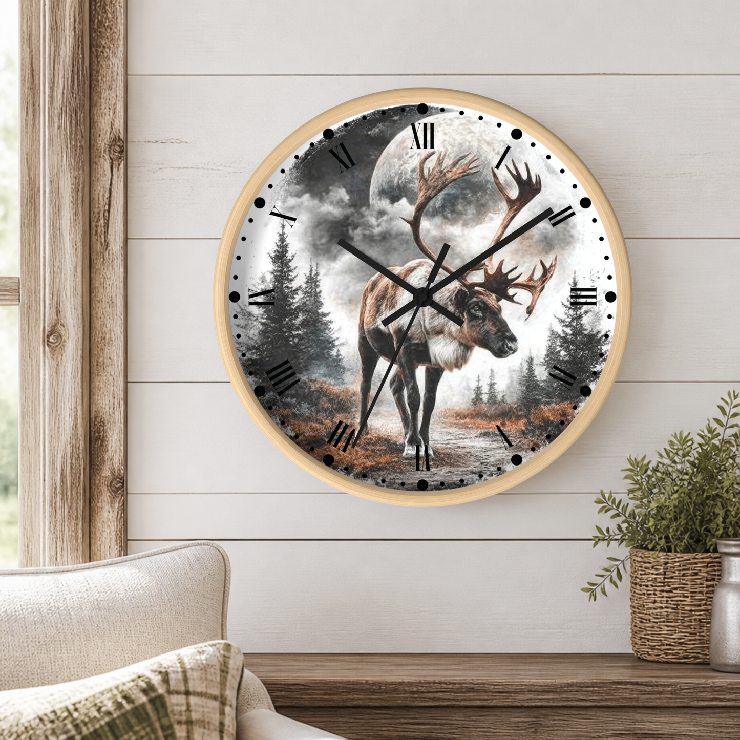 Round wall clock with a light wood frame featuring a detailed illustration of a reindeer under a full moon in a forest, mounted on a white shiplap wall above a wooden mantel with a plant.