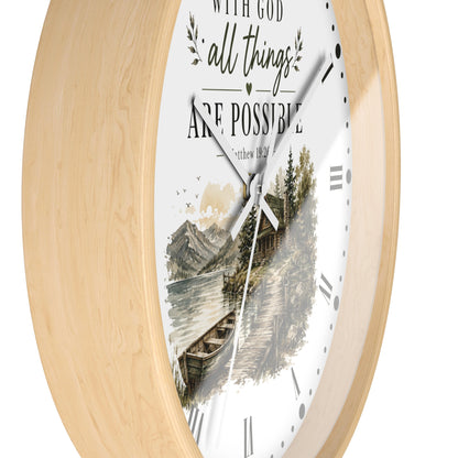 A round wall clock with a light natural wood frame and a white dial featuring a scenic mountain lake illustration and the text 'WITH GOD all things ARE POSSIBLE' and 'Romans 8:28'.