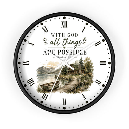 A round wall clock with a black frame and a white face featuring Roman numerals, black text reading 'WITH GOD all things ARE POSSIBLE Matthew 19:26', and a scenic illustration of a lakeside cabin and mountains near the bottom.