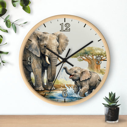 Round wall clock with a light wood frame and a safari-themed elephant illustration on the dial, shown hanging on a white wall above a wooden surface with small plants nearby.