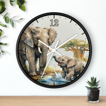 Round wall clock with a black frame and a printed scene of an adult and baby elephant at a watering hole, shown hanging on a white wall above a wooden surface with small plants.
