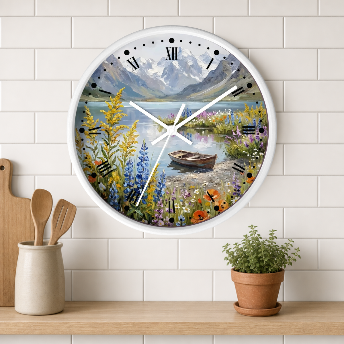 A round wall clock with a white frame and a scenic landscape print of a mountain lake, mounted on a white subway tile wall above a wooden shelf with a small potted plant and wooden utensils.