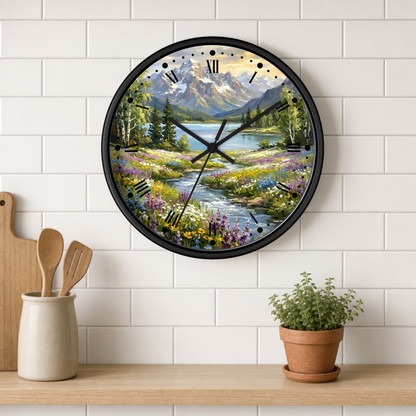 A round wall clock with a black frame and a scenic mountain landscape print, mounted on a white subway tile wall above a wooden shelf with kitchen utensils and a potted plant.