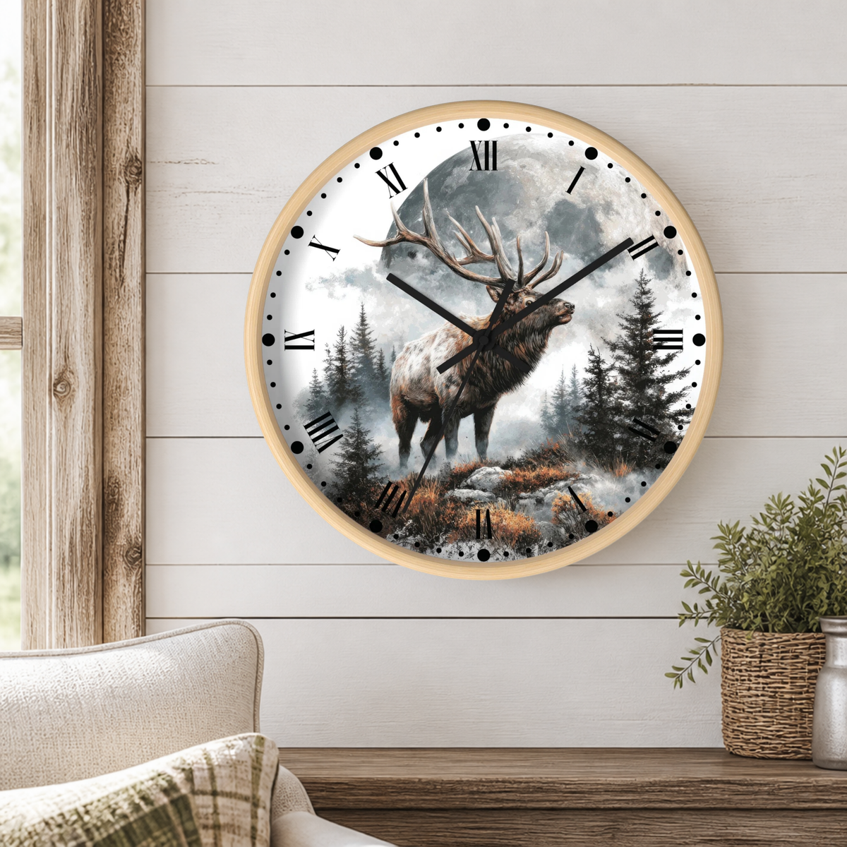 A round wall clock with a light wood frame hangs on a white shiplap wall above a wooden table. The clock face features a detailed illustration of a large deer standing in a misty forest under a full moon.