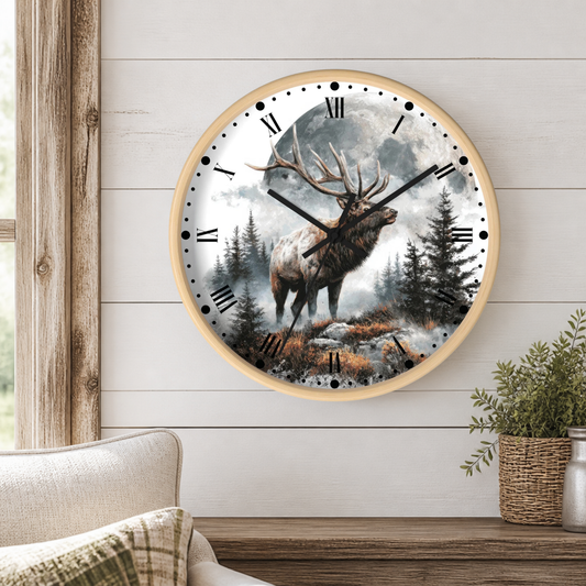 A round wall clock with a light wood frame hangs on a white shiplap wall above a wooden table. The clock face features a detailed illustration of a large deer standing in a misty forest under a full moon.