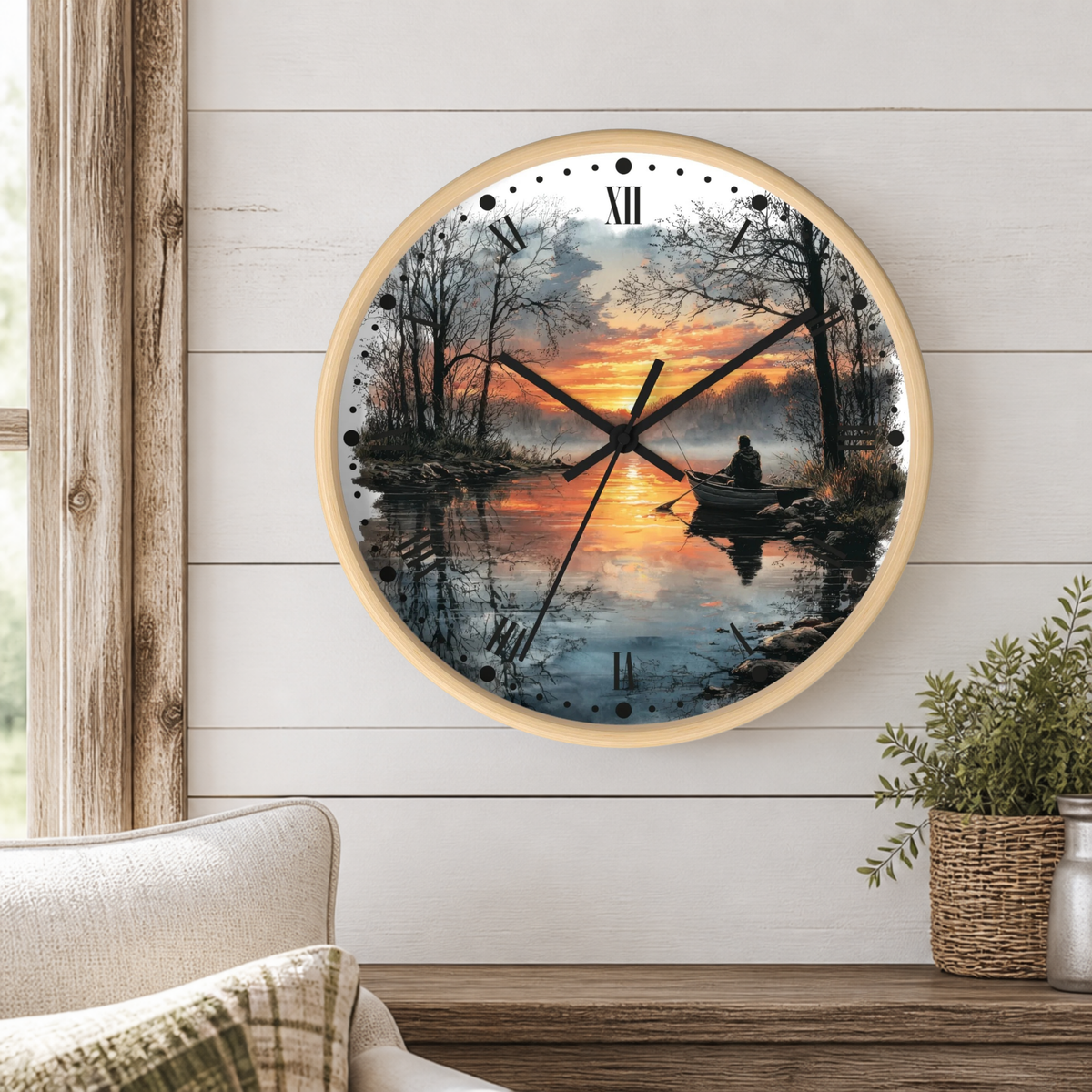 A round wall clock with a light wood frame hangs on a white shiplap wall above a wooden table. The clock face features a scenic sunset landscape print of a person rowing on a calm lake, with black Roman numerals and hands.
