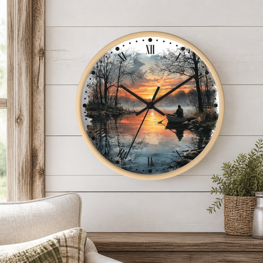 A round wall clock with a light wood frame hangs on a white shiplap wall above a wooden table. The clock face features a scenic sunset landscape print of a person rowing on a calm lake, with black Roman numerals and hands.