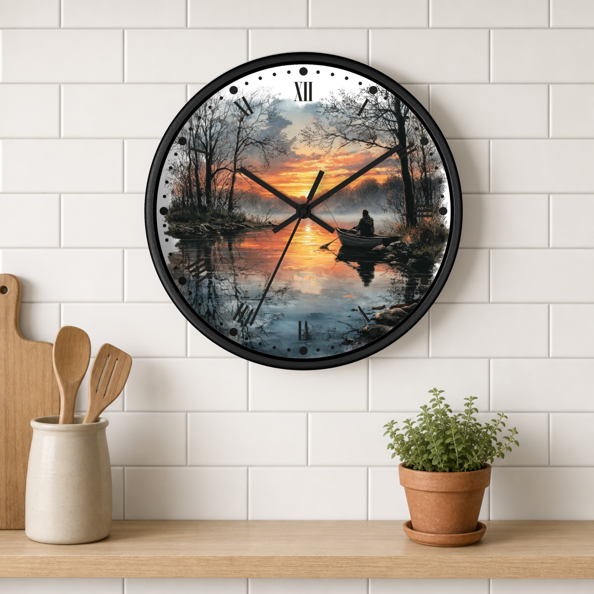 A round wall clock with a black frame and a scenic lake sunset print, mounted on a white subway tile wall above a wooden shelf with kitchen utensils and a potted plant.