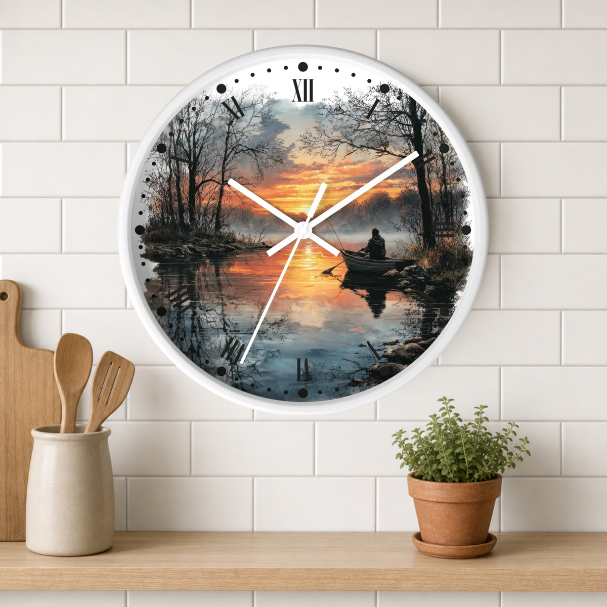 Round wall clock with a white frame and a scenic sunset landscape print of a person rowing on a lake, mounted on a white subway tile wall above a wooden shelf with kitchen utensils and a potted plant.