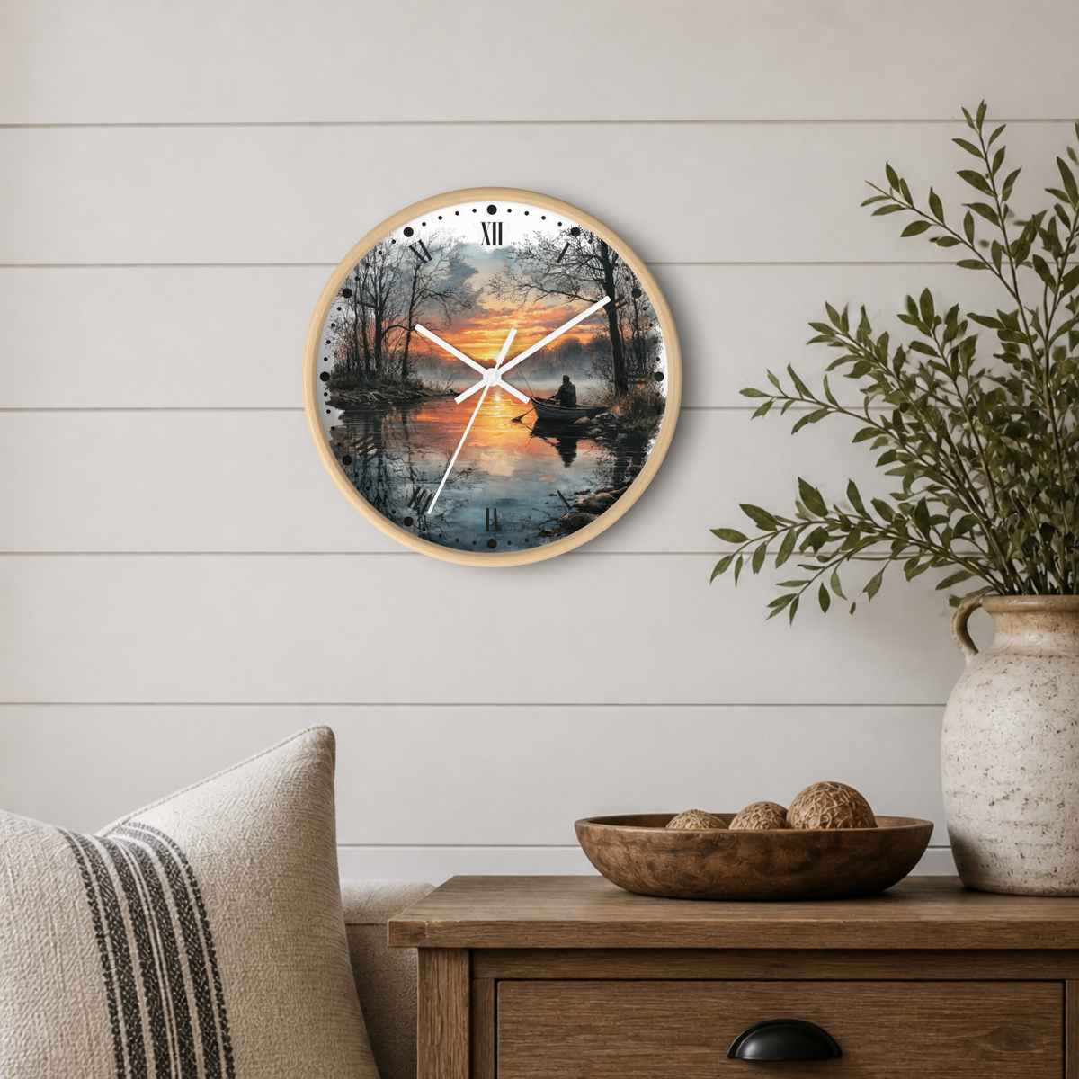 Round wall clock with a natural wood frame and a scenic sunset lake print, styled on a white shiplap wall above a wooden side table with a vase and bowl.