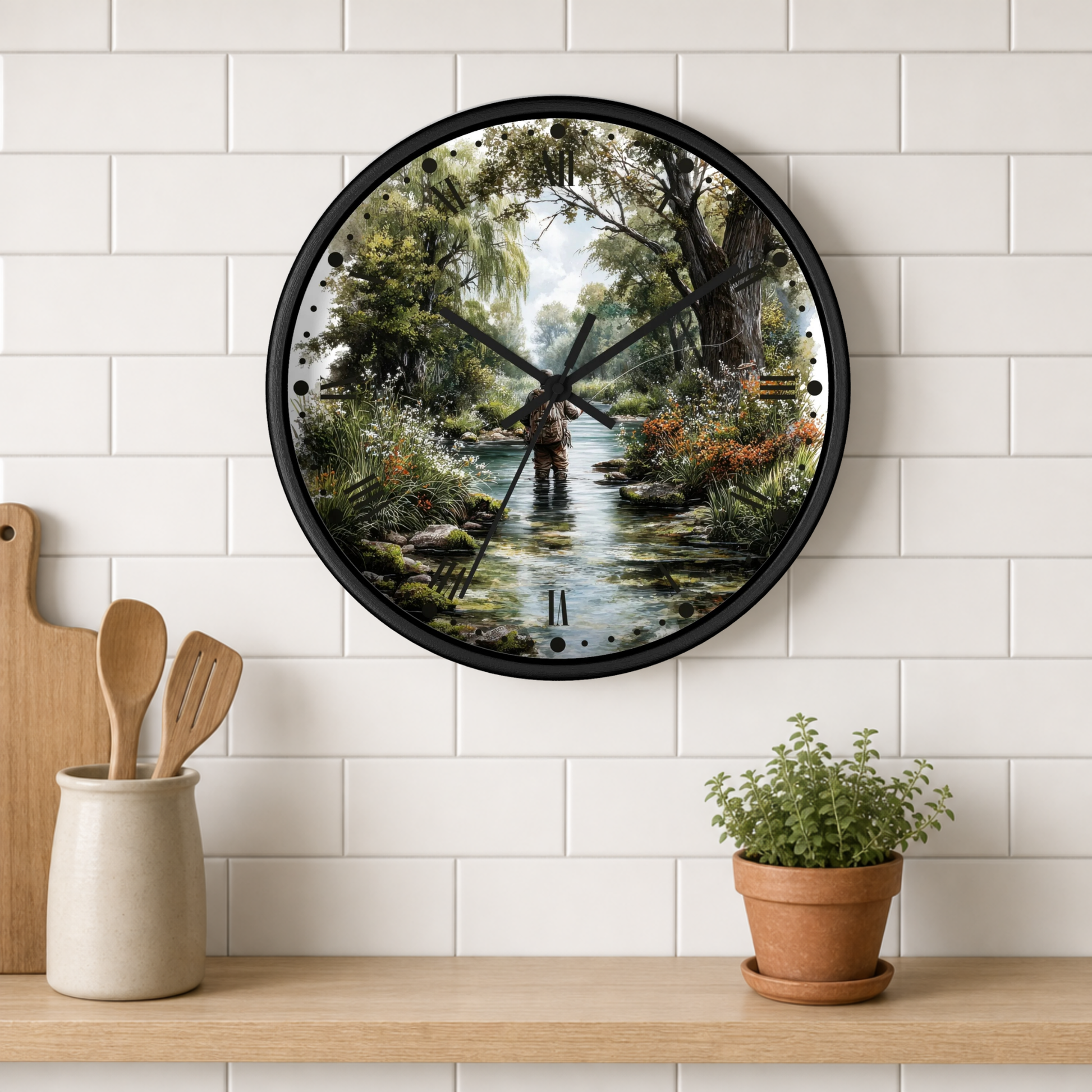 A round wall clock with a black frame and a scenic forest stream illustration on the face, mounted on a white subway tile wall above a wooden shelf with kitchen utensils and a potted plant.