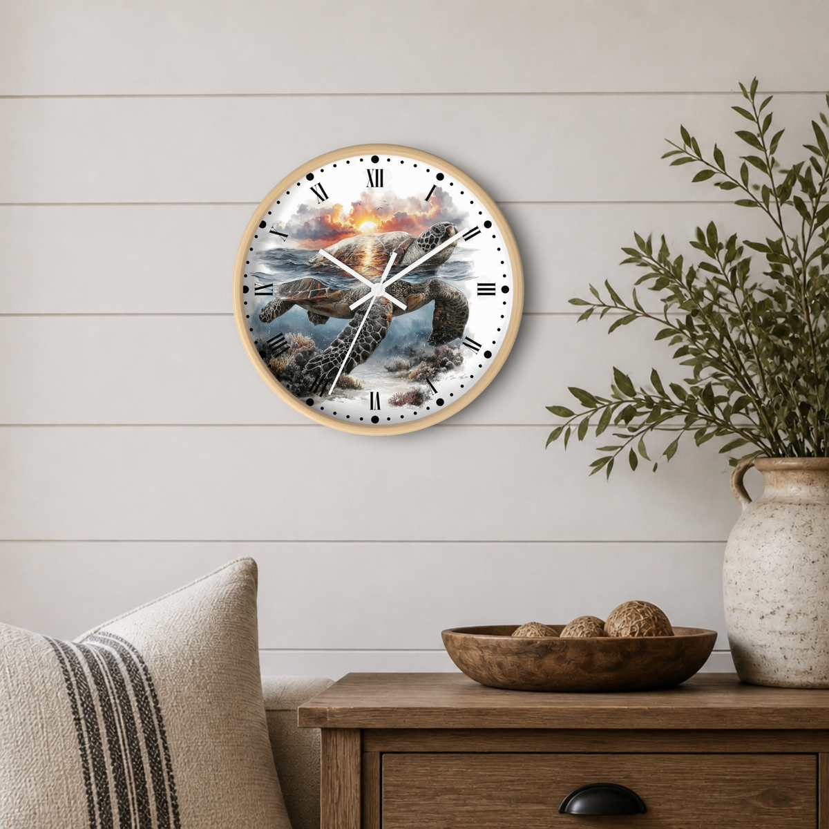 A round wall clock with a light wood frame and a detailed sea turtle illustration on the face, mounted on a white shiplap wall above a wooden side table with a vase and bowl.