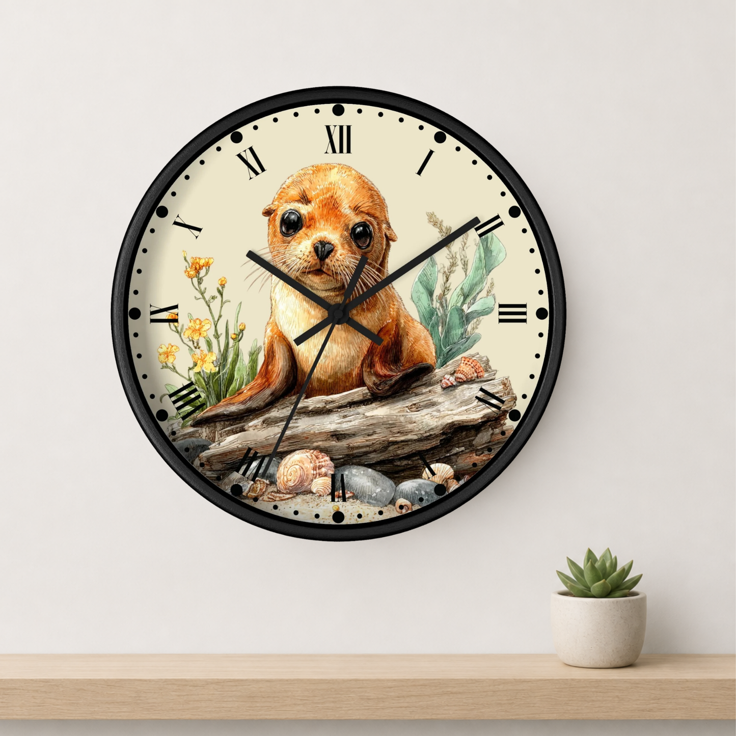 A round wall clock with a black frame and a cream-colored face, featuring a watercolor illustration of a brown seal on a log with flowers and shells. The clock is mounted on a light gray wall above a wooden shelf with a small potted succulent.