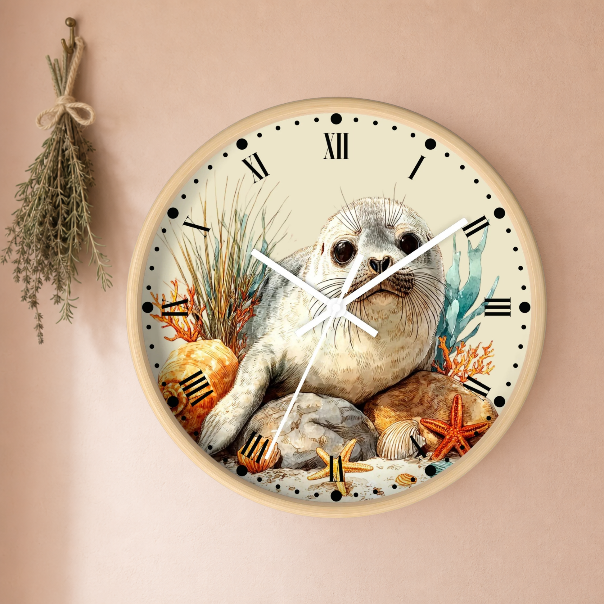 Round wall clock with a beige frame and a detailed illustration of a seal on an ocean beach scene, mounted on a beige wall with a dried herb sprig hanging to the left.