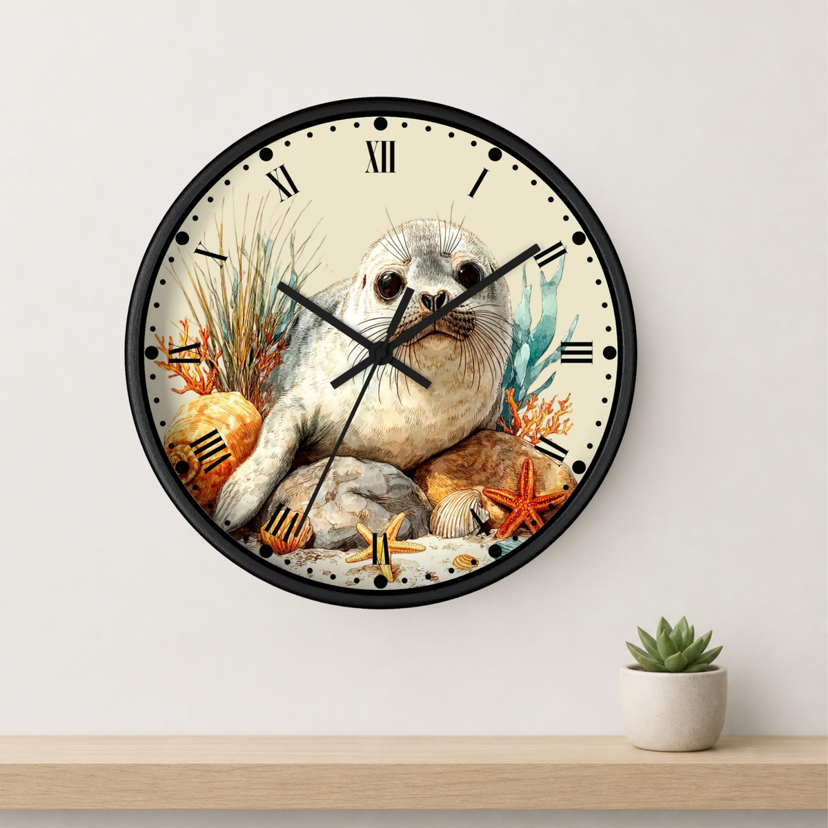 A round wall clock with a black frame and a printed illustration of a seal sitting among rocks, coral, and starfish on a cream face. The clock is mounted on a light wall above a wooden shelf with a small potted succulent.