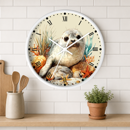 A round wall clock with a white frame and a detailed illustration of a seal sitting among sea plants and starfish on the face, mounted on a white subway-tile wall above a wooden shelf with kitchen utensils and a potted plant.
