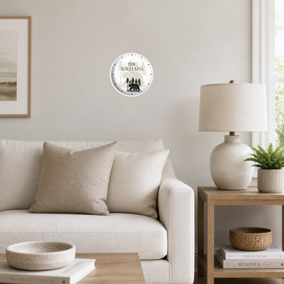 A round wall clock with a distressed white face and black text reading 'THE Williams' is mounted on a light beige wall in a styled living room setting with a sofa, side table, and lamp.