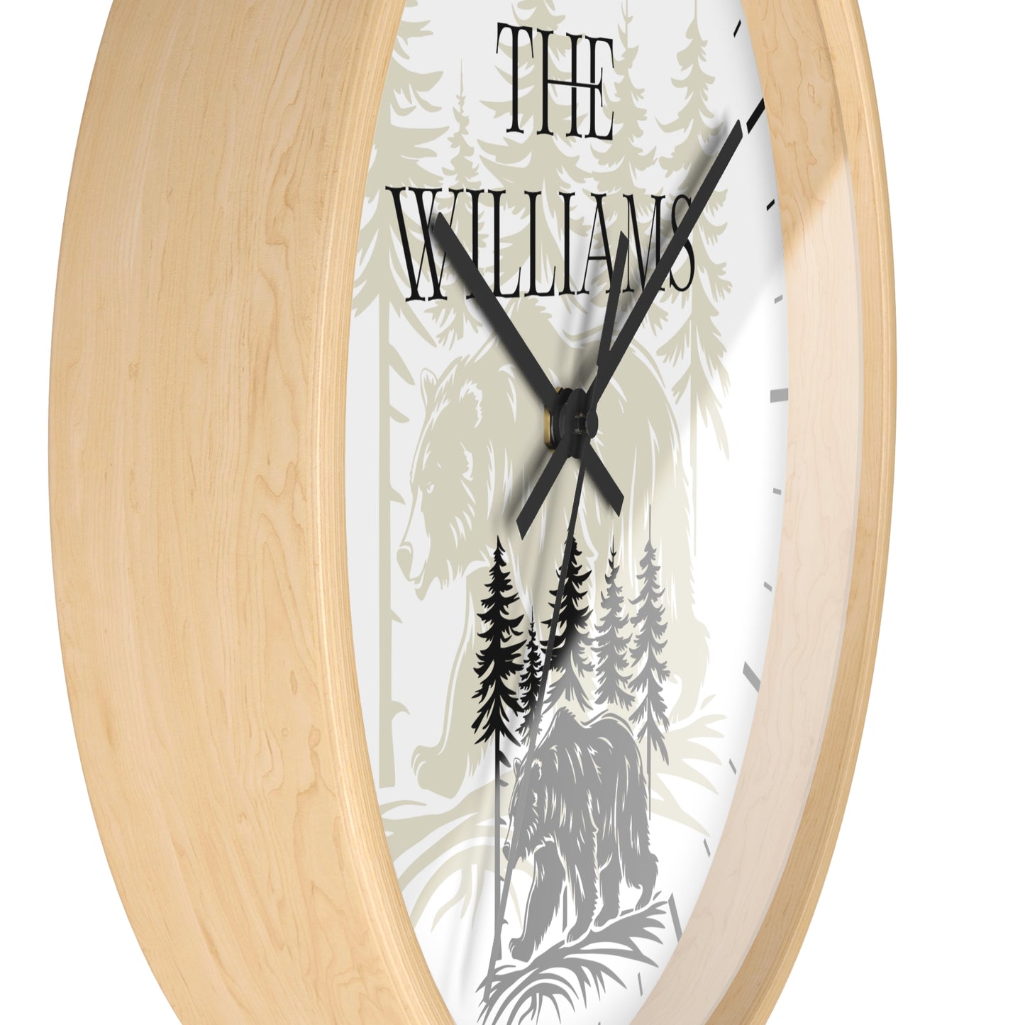 A close-up of a round wall clock with a light natural wood frame and a white face featuring a forest illustration with the text 'THE WILLIAMS' and black hands.