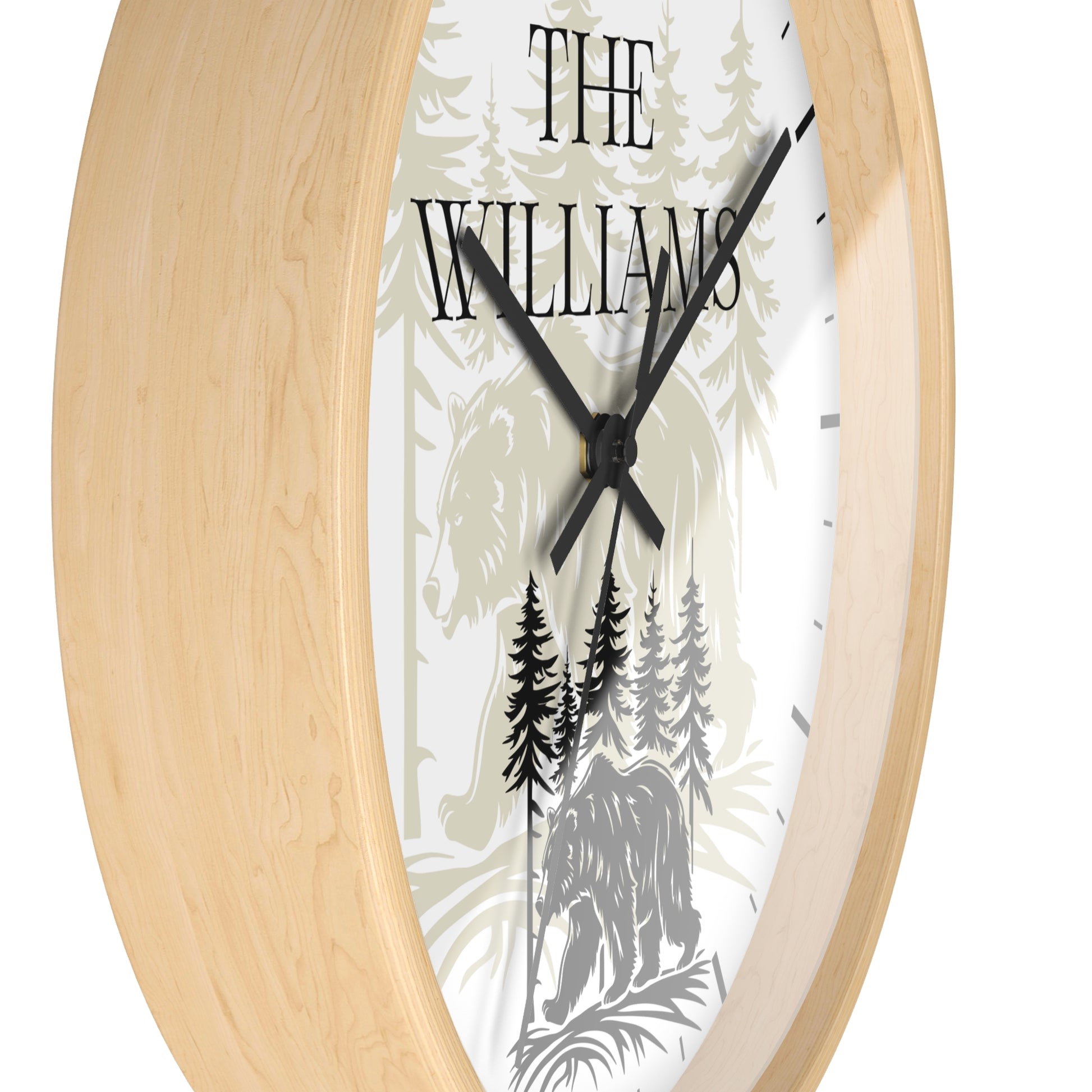 A close-up of a round wall clock with a light natural wood frame and a white face featuring a forest illustration with the text 'THE WILLIAMS' and black hands.