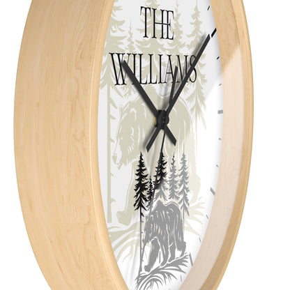 A close-up of a round wall clock with a light natural wood frame and a white face featuring a forest illustration with the text 'THE WILLIAMS' and black hands.