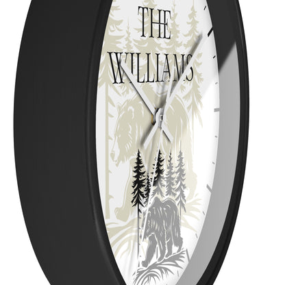 A close-up of a round wall clock with a black frame and a custom white dial featuring a forest design with the text 'THE WILLIAMS' and the names 'M. & J.