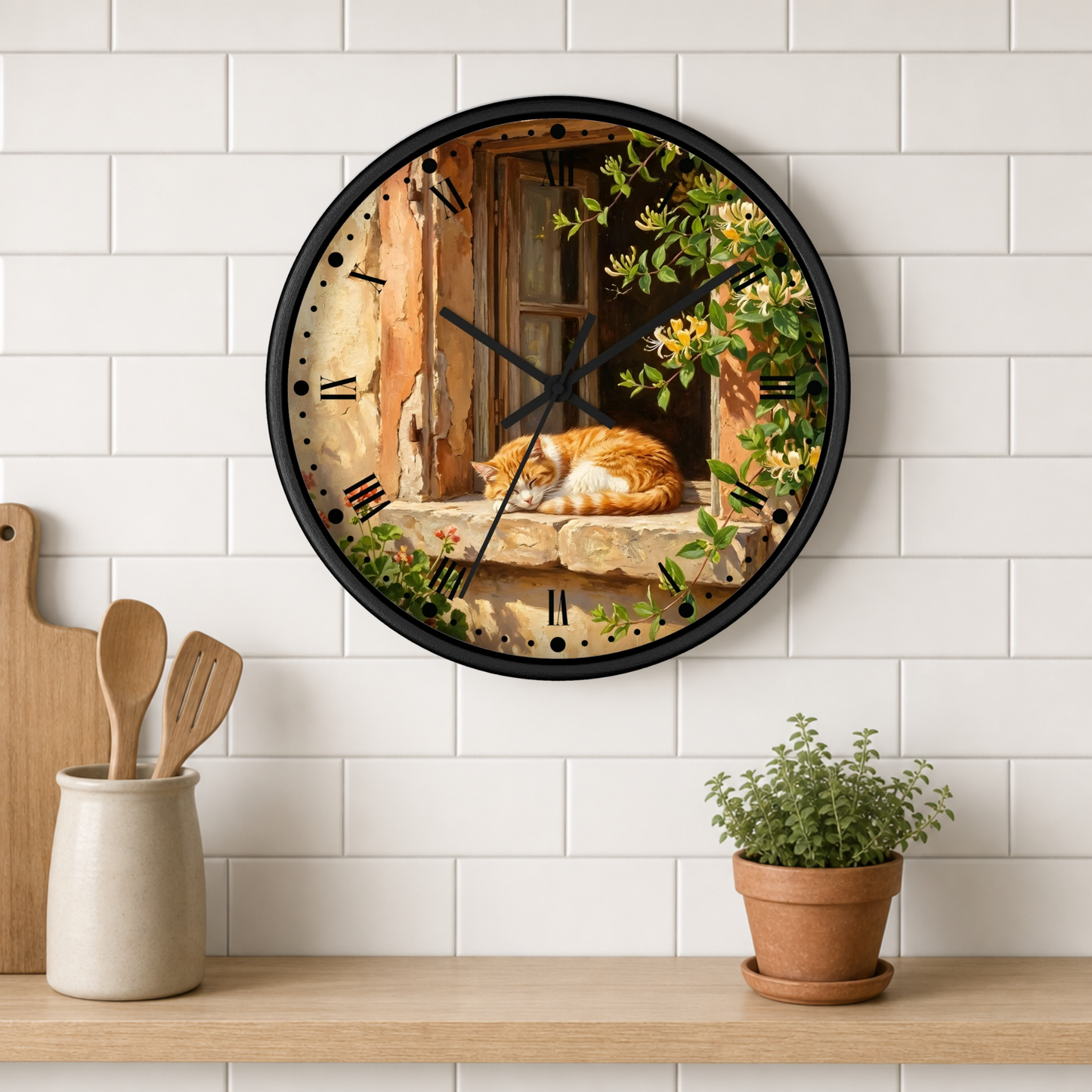 A round wall clock with a black frame hangs on a white subway-tile kitchen wall above a wooden shelf. The clock face features a scenic print of an orange cat sleeping by a rustic window with green vines.