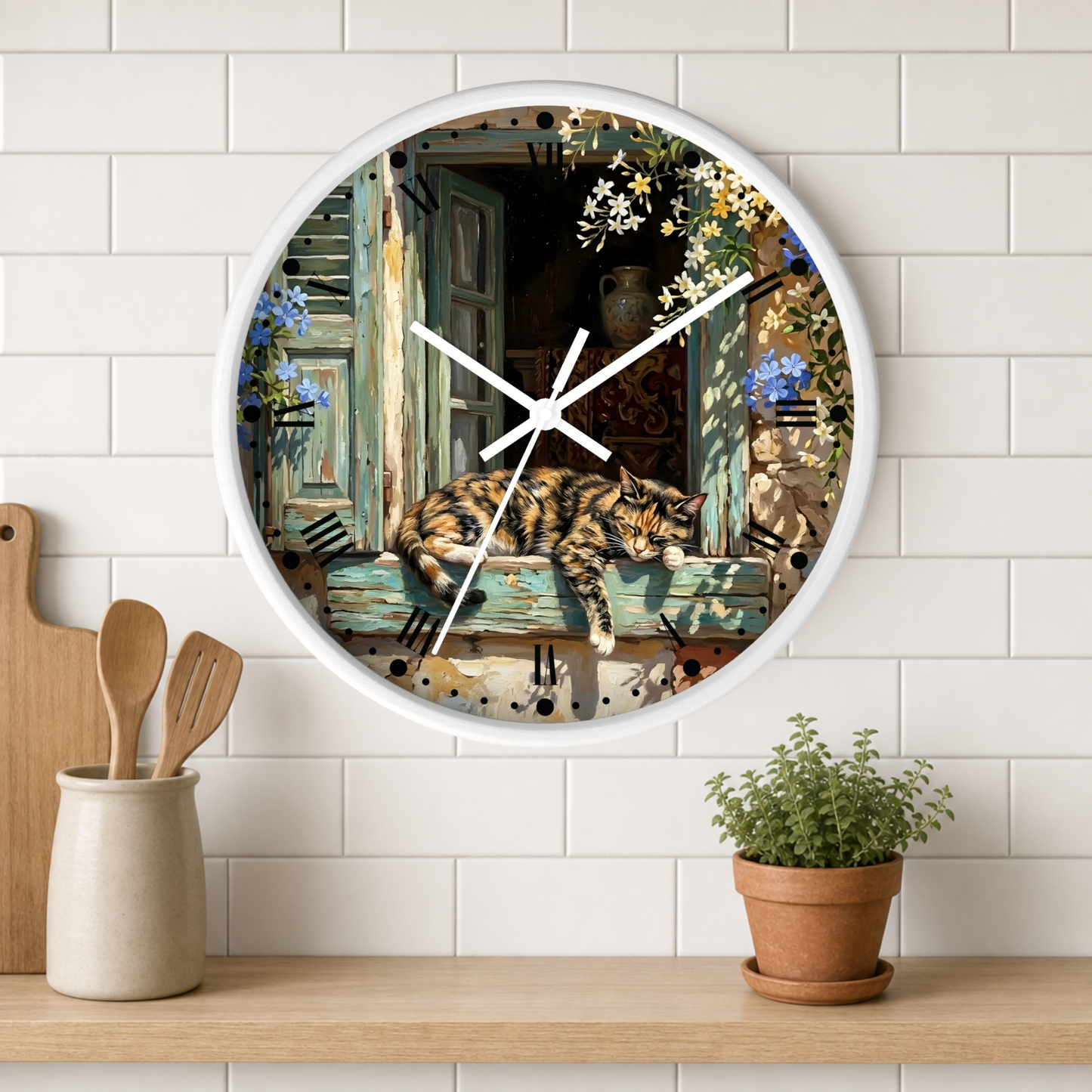 A round wall clock with a white frame hangs on a white subway tile kitchen wall above a wooden shelf. The clock face features a detailed illustration of a tortoiseshell cat sleeping on a weathered green wooden window sill, surrounded by flowers and kitchen utensils.