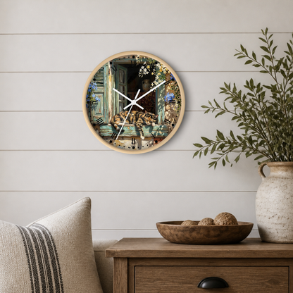 Round wall clock with a light wood frame and a detailed illustration of a cat lounging on a windowsill, styled on a white shiplap wall above a wooden side table with a vase and bowl.