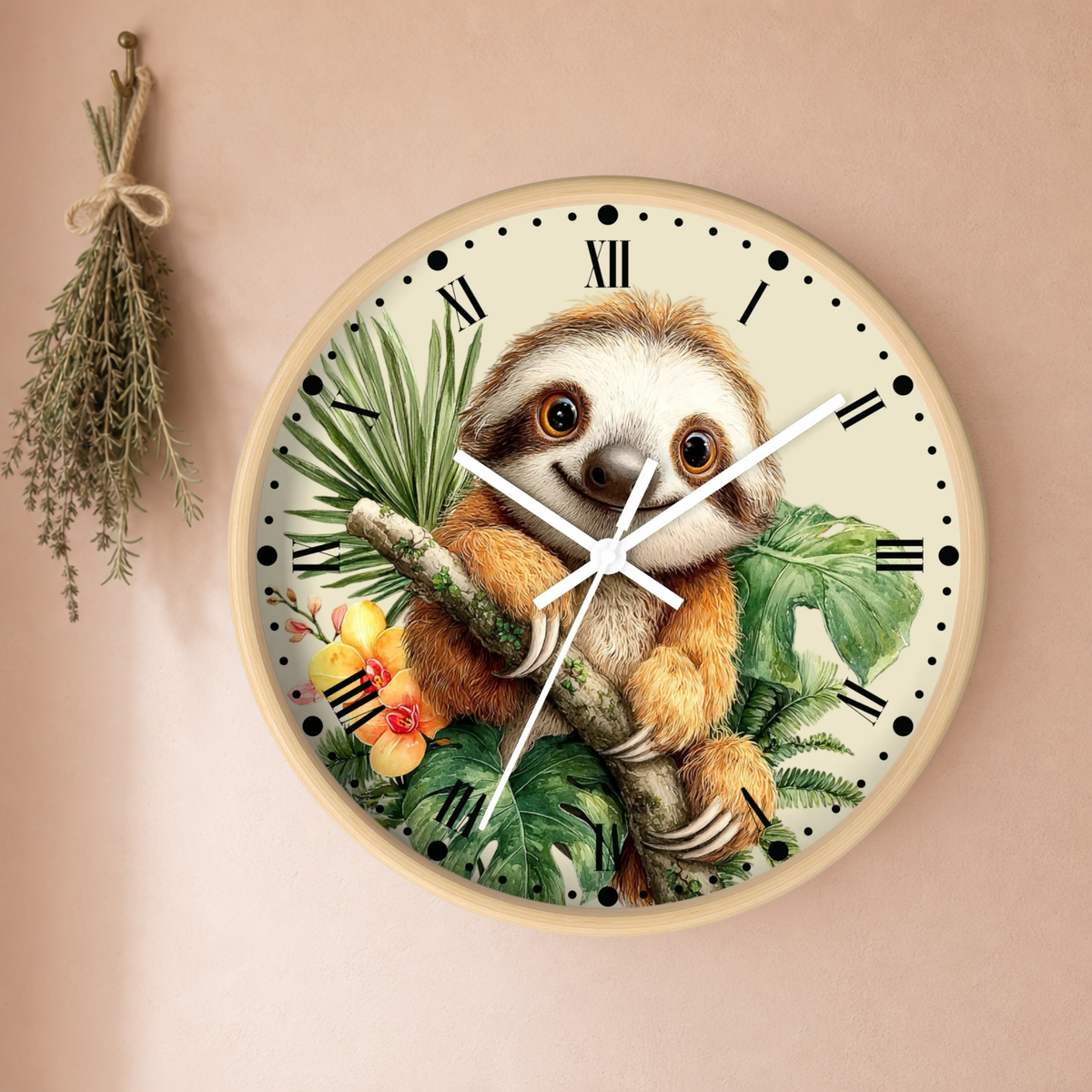 A round wall clock featuring a detailed illustration of a smiling sloth among tropical green leaves and small yellow-orange flowers. The clock has a light wood-toned frame, black Roman numerals, and white hands, mounted on a warm beige wall with a dried herb sprig hanging to the left.
