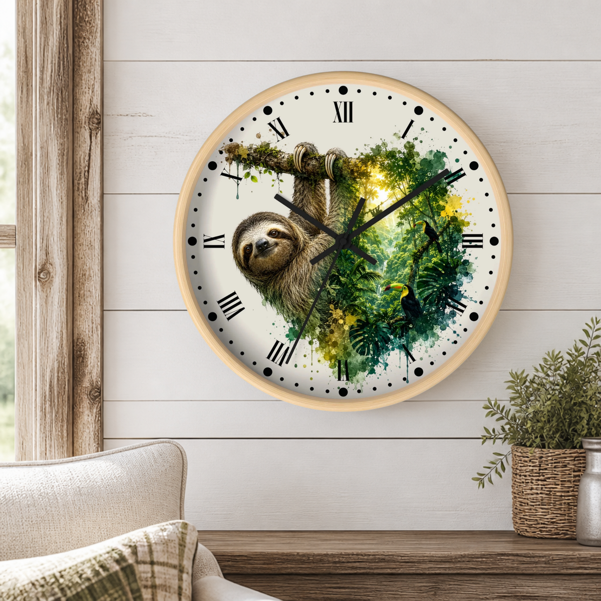A round wall clock with a light wood frame hangs on a white shiplap wall above a wooden table. The clock face features a sloth illustration over a green and yellow jungle watercolor design, with black Roman numerals and hands.